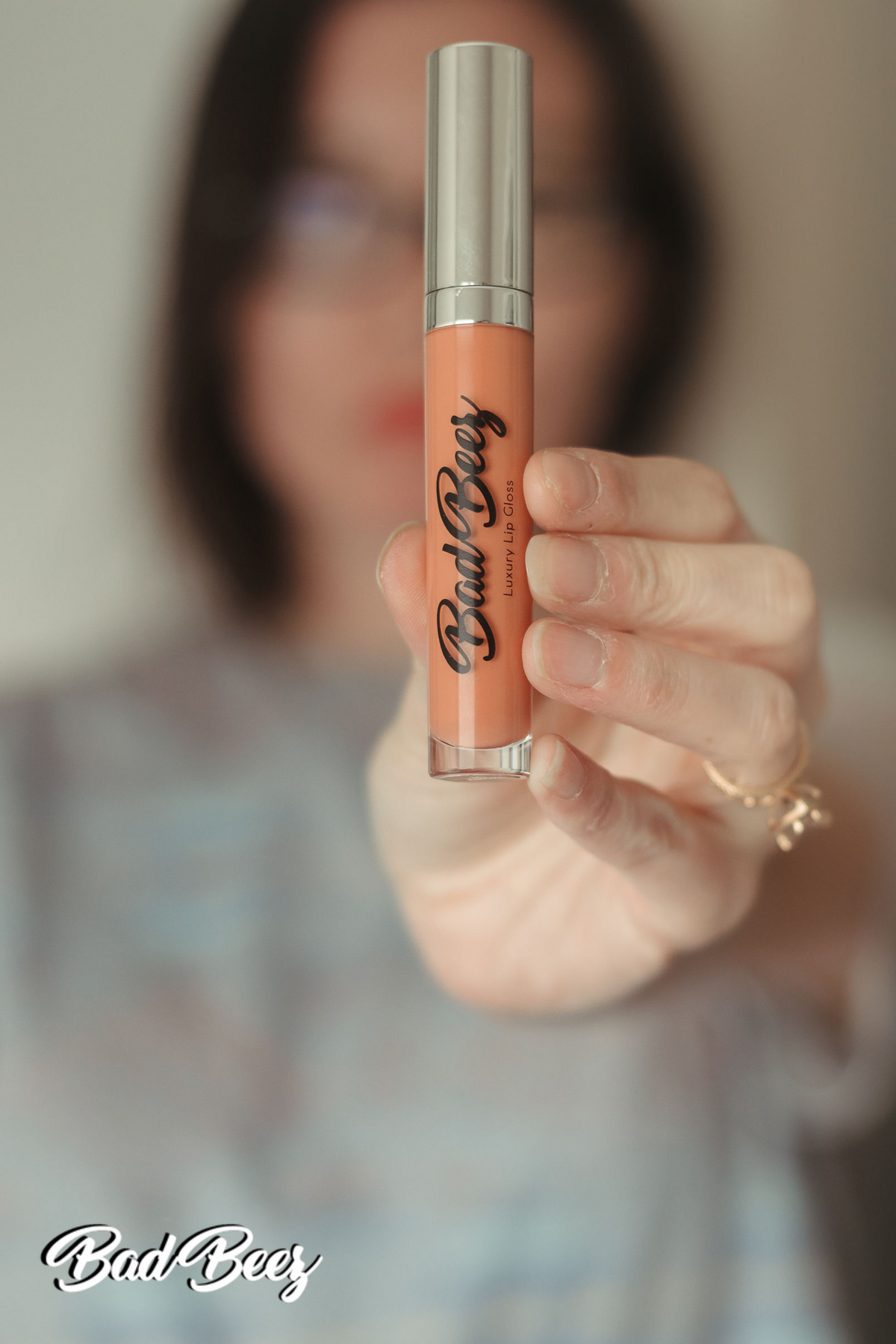 girl with glasses holding up shiny lip gloss